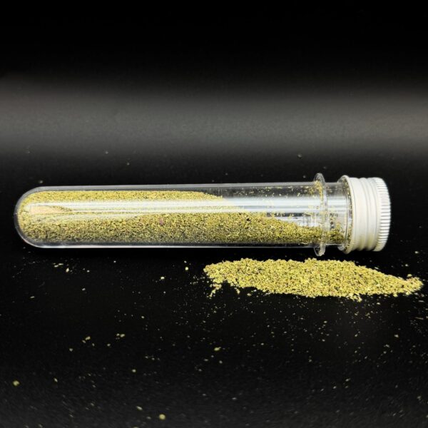 Clear plastic test tube with a white cap tipped over, spilling yellow-green granular powder onto a black surface.