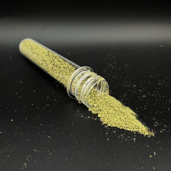 A clear glass vial tipped over, spilling fine gold powder across a dark surface.