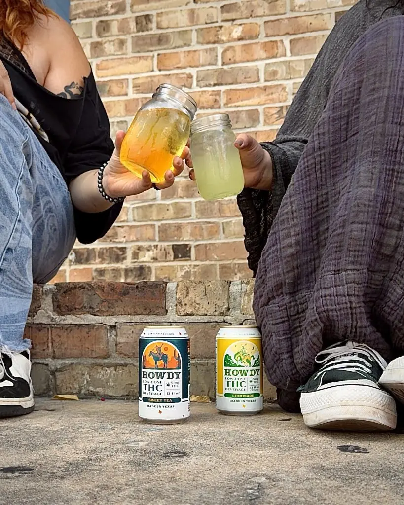 Two friends toast mason jars of iced tea and lemonade beside HOWDY low-dose THC seltzer cans in sweet tea and lemonade flavors.