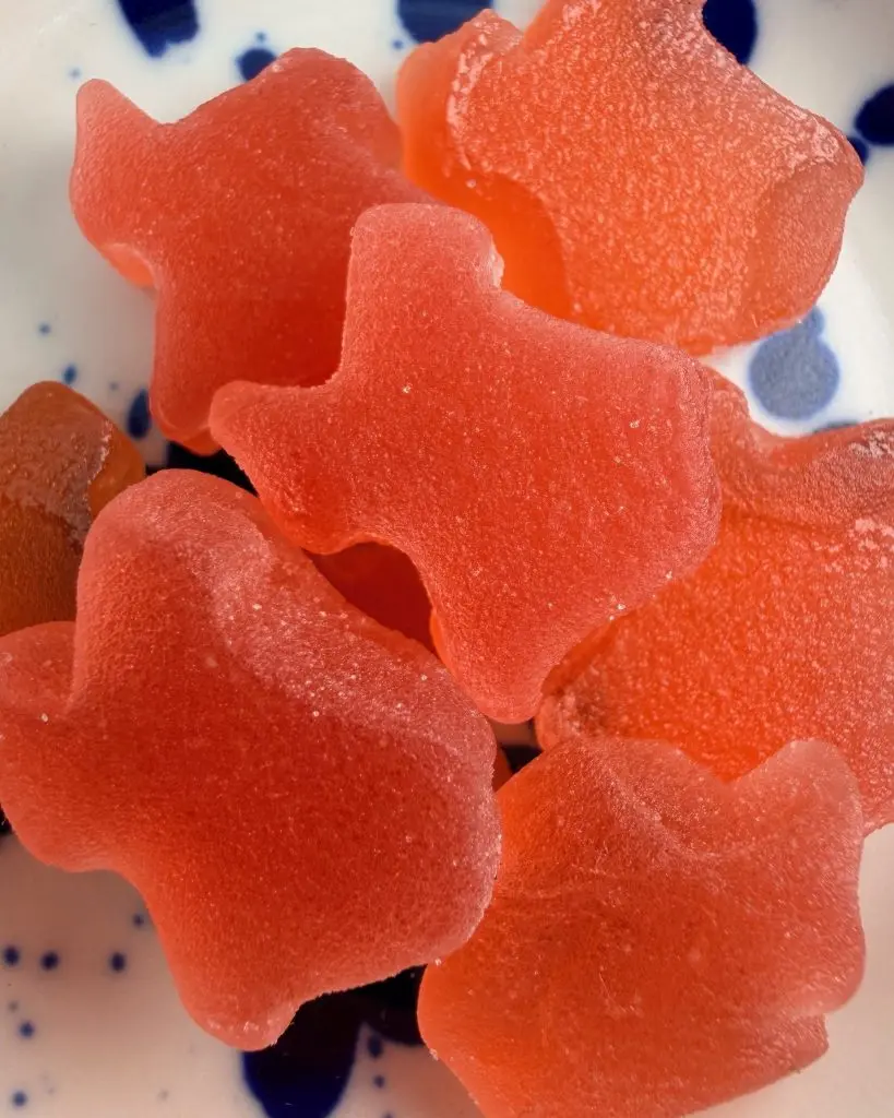 A close-up stack of red and orange THC gummies on a white plate with cobalt-blue speckles.